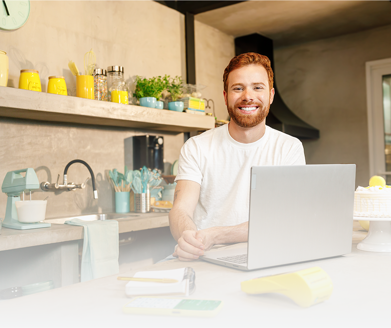 Homem sentado em frente a mesa com notebook, celular e maquininha PagBank