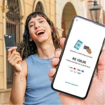 Uma pessoa segura um smartphone que exibe uma tela de pagamento por aproximação no valor de R$ 100, enquanto outra pessoa segura um cartão físico PagBank ao fundo, em uma área externa com prédios.