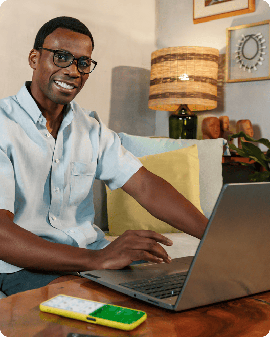 Pessoa sentada usando um notebook sobre mesa de madeira, com smartphone ao lado, sugerindo trabalho ou gestão de atividades.