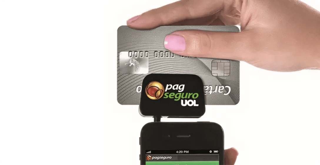 Mão segurando leitor de cartão de crédito com tarja, inovação do PagBank em 2013.